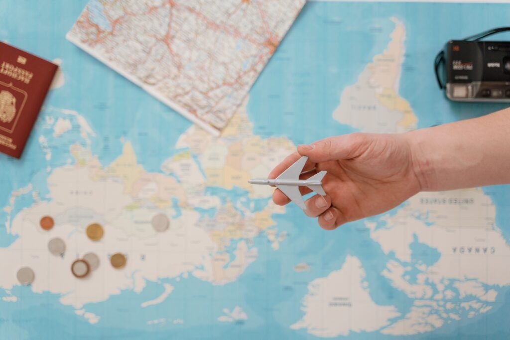 Hand holding a toy airplane over a world map with a passport and coins